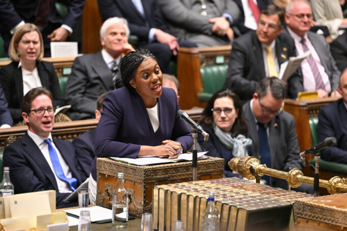 Badenoch offers support to fund warfare through welfare cuts Politician in a purple blazer speaks into a microphone at a ceremonial desk in a parliamentary chamber, with lawmakers watching.
