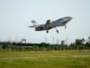 Italian jets fly with Turkish drones in K-SWARM live trial Stealth fighter jet lifting off from a runway, low above a grassy field with a fence in the foreground.