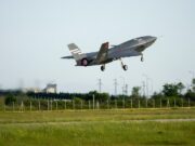 Italian jets fly with Turkish drones in K-SWARM live trial Stealth fighter jet lifting off from a runway, low above a grassy field with a fence in the foreground.