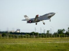 Italian jets fly with Turkish drones in K-SWARM live trial Stealth fighter jet lifting off from a runway, low above a grassy field with a fence in the foreground.