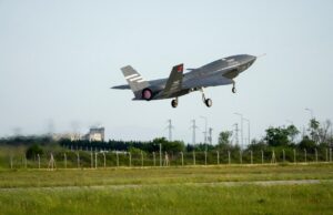 Stealth fighter jet lifting off from a runway, low above a grassy field with a fence in the foreground.