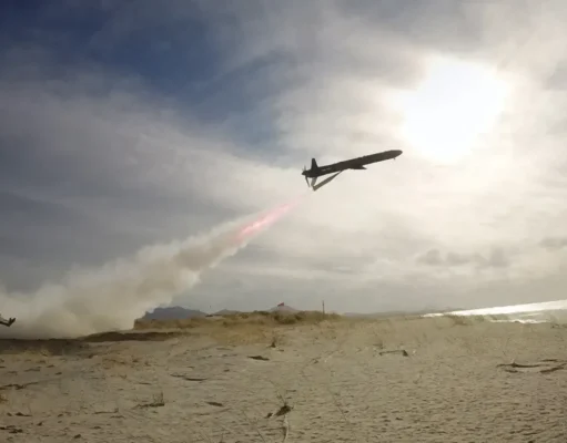 Air tanker plane releasing red retardant over a sandy beach as smoke rises from a ground fire nearby