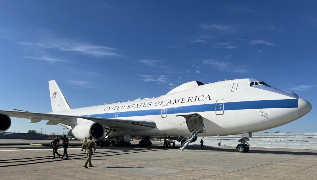 Air Force One parked on a sunny tarmac with stairs deployed to the door and crew nearby