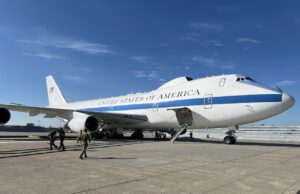 Air Force One parked on a sunny tarmac with stairs deployed to the door and crew nearby