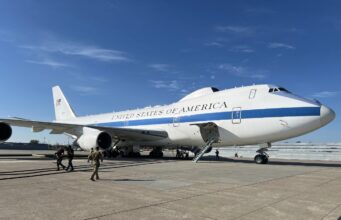 Air Force One parked on a sunny tarmac with stairs deployed to the door and crew nearby