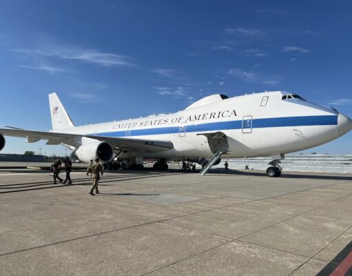 Air Force One parked on a sunny tarmac with stairs deployed to the door and crew nearby