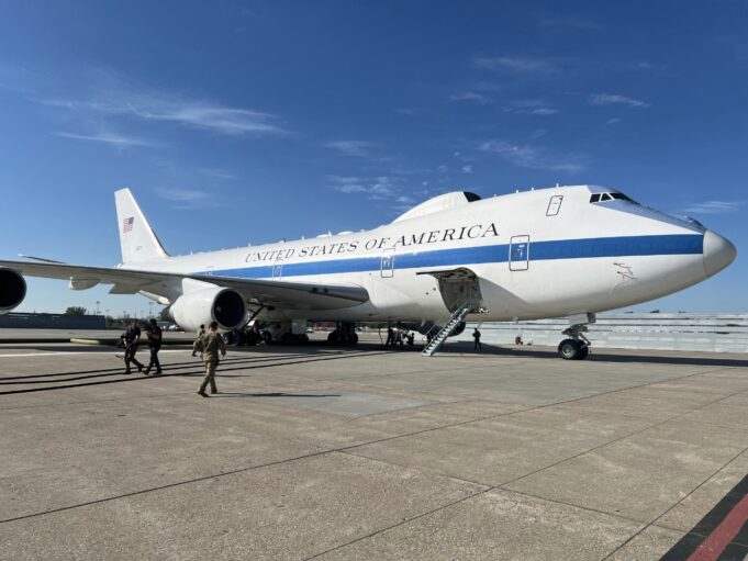Air Force One parked on a sunny tarmac with stairs deployed to the door and crew nearby