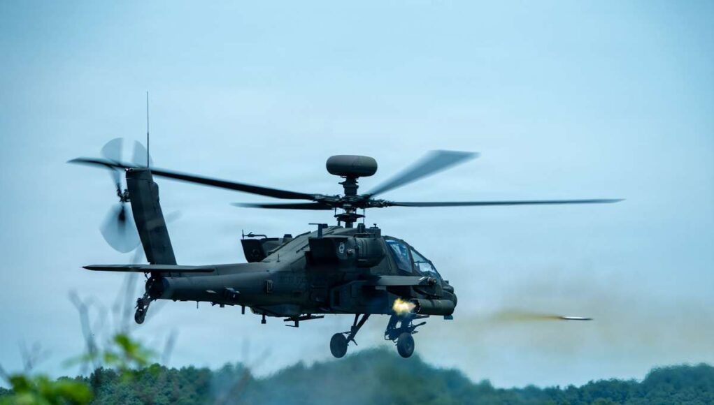9741892 Military attack helicopter in mid-flight firing a missile over a forested area