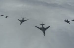 Six military aircraft flying in a loose formation across a cloudy sky.