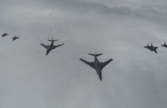 Six military aircraft flying in a loose formation across a cloudy sky.