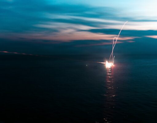 Firework explosion on the water at dusk, long-exposure light trail over the dark sea.