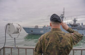 NATO kicks off huge BALTOPS drill to deter Russia Sailor in camouflage uniform saluting as a gray warship with the number 05 passes by on the water.