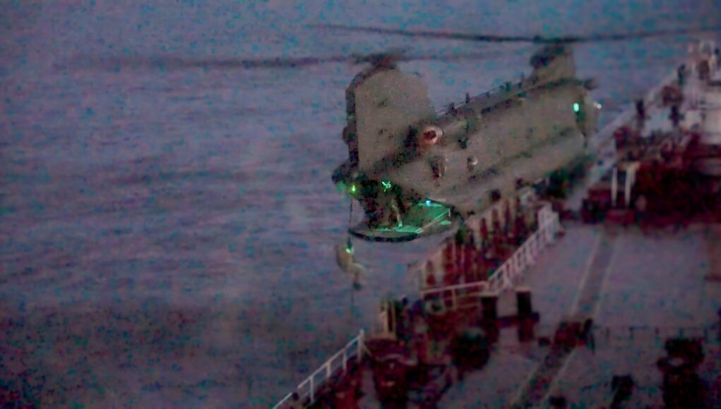 BOARDING Blurred night photo of a seafront pier with a concrete extension over water and green lights along its edge.