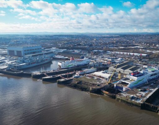 Aerial view of a harbor with two large white Stena Line ferries docked at the quay and industrial buildings nearby under a blue, cloudy sky.