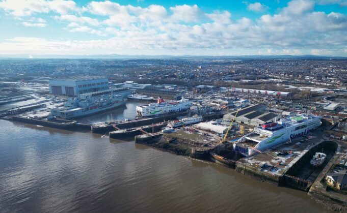 Balaena buys Cammell Laird owner in UK shipyard shake-up Aerial view of a harbor with two large white Stena Line ferries docked at the quay and industrial buildings nearby under a blue, cloudy sky.