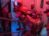 British forces board Russian shadow fleet tanker near UK Special-ops style operator in full gear pointing a weapon through a doorway in a dim, red-and-blue lit stairwell.