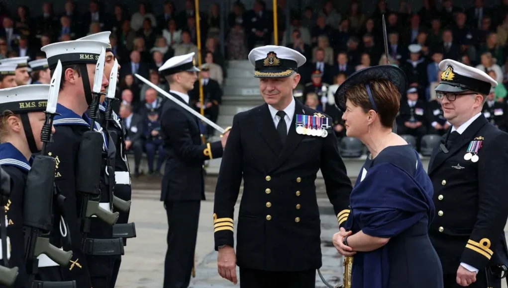FRPUE-20260612-ZE0207-007 Naval officers in dress uniforms stand in formation as a woman in a dark dress speaks with them during a formal ceremony.