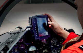 Red Arrows get Inzpire GECO system for 2026 season Pilot in a red flight suit uses a rugged tablet-style display in the fighter jet cockpit, surrounded by instrument gauges.