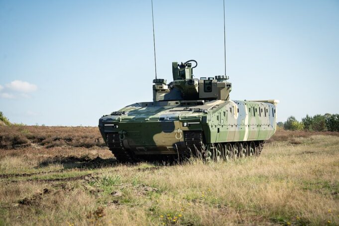 Armored military tank on a grassy field under a clear blue sky, facing left.