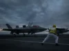 Two fighter jets parked on a dark aircraft carrier deck at dusk, with a crew member in a yellow vest guiding them.