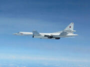 White military cargo aircraft with a red star on the tail flying over a clear blue sky, four engines visible under the wings.
