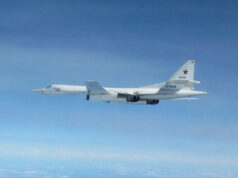 White military cargo aircraft with a red star on the tail flying over a clear blue sky, four engines visible under the wings.