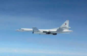 White military cargo aircraft with a red star on the tail flying over a clear blue sky, four engines visible under the wings.