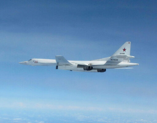 White military cargo aircraft with a red star on the tail flying over a clear blue sky, four engines visible under the wings.