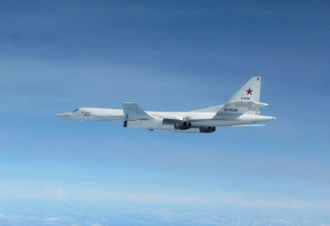 White military cargo aircraft with a red star on the tail flying over a clear blue sky, four engines visible under the wings.
