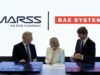 MARSS picked to run command brain of BAE drone-killer Three businesspeople in suits signing documents at a table, with MASS and BAE SYSTEMS logos in the bright backdrop.