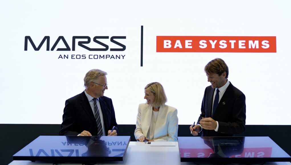 MARSS x BAE - Eurosatory 2026 -2317 Three businesspeople in suits signing documents at a table, with MASS and BAE SYSTEMS logos in the bright backdrop.