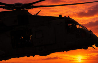 Royal Navy Merlin helicopter crashes in Devon Silhouette of a military helicopter flying at sunset against a fiery orange sky.