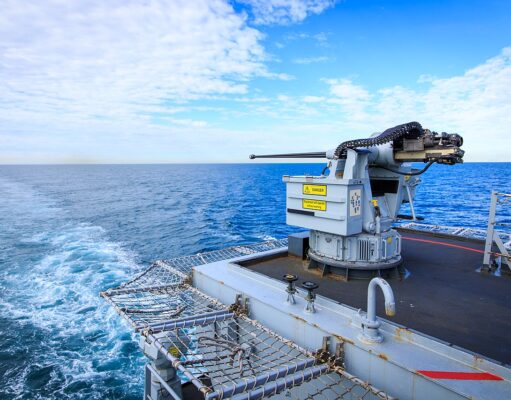 Naval gun mounted on a ship's deck with the open ocean and blue sky in the background.