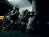 Special forces operators in full tactical gear crouch and aim rifles in a dim corridor of a vessel or building.