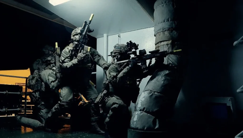 Royal Marines Commandos conduct boarding training during Exercise Hyperion Storm Special forces operators in full tactical gear crouch and aim rifles in a dim corridor of a vessel or building.