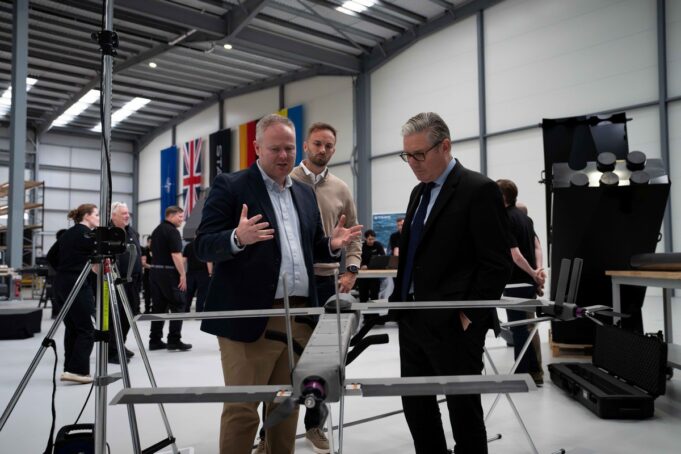 STARK debuts Cascade and Gambit drones with UK partner Three men in a workshop inspect a large drone mounted on a stand, with flags along the wall in the background.