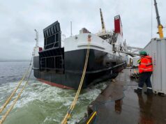 Glen Rosa’s engine roars to life at Ferguson Marine Large vessel docked at a quay with thick mooring lines; a worker in a high-visibility jacket and hard hat stands on the dock nearby.