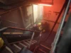 RFA Lyme Bay reaches Cyprus ahead of Hormuz mission Firefighters in yellow turnout gear with breathing apparatus crouch in a smoke-filled ship corridor under red emergency lighting near a doorway.