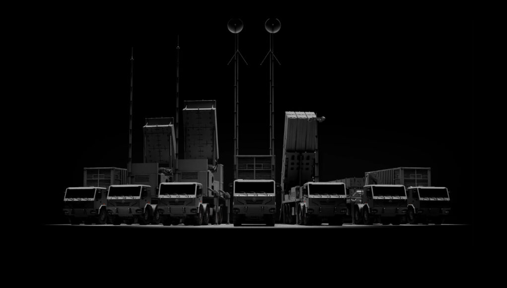 Trident air defence system Row of large trucks with tall antenna masts silhouetted against a dark background, forming a straight line.