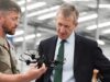 New Defence Secretary opens huge drone centre in Swindon Military personnel in camouflage hands a tactical vest to a businessman in a suit inside a hangar, as they converse.