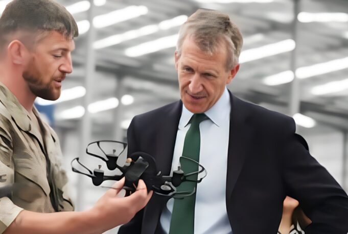 New Defence Secretary opens huge drone centre in Swindon Military personnel in camouflage hands a tactical vest to a businessman in a suit inside a hangar, as they converse.