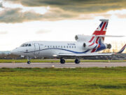 White business jet with Union Jack tail taxiing on a runway under a cloudy sky