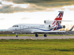 White business jet with Union Jack tail taxiing on a runway under a cloudy sky