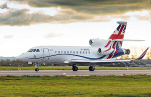 White business jet with Union Jack tail taxiing on a runway under a cloudy sky