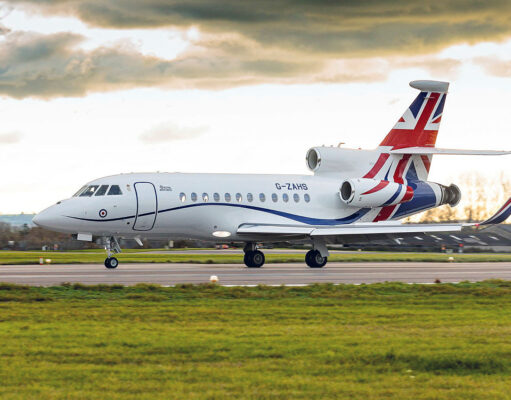 White business jet with Union Jack tail taxiing on a runway under a cloudy sky