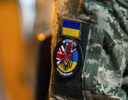 Military jacket with unit patches: Ukrainian flag patch above a round Interflex patch featuring a stylized red creature over a blue-yellow background.
