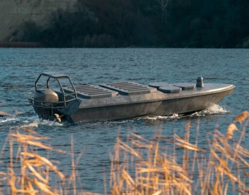 Small aluminum motorboat gliding on a blue lake with a rocky shore in the background, grasses in the foreground.