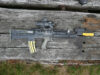 Assault rifle with scope and foregrip lying on weathered wooden planks.