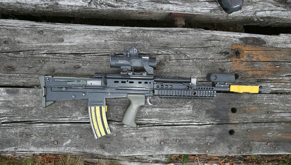 Assault rifle with scope and foregrip lying on weathered wooden planks.