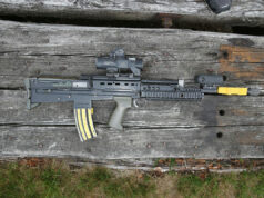 Assault rifle with scope and foregrip lying on weathered wooden planks.
